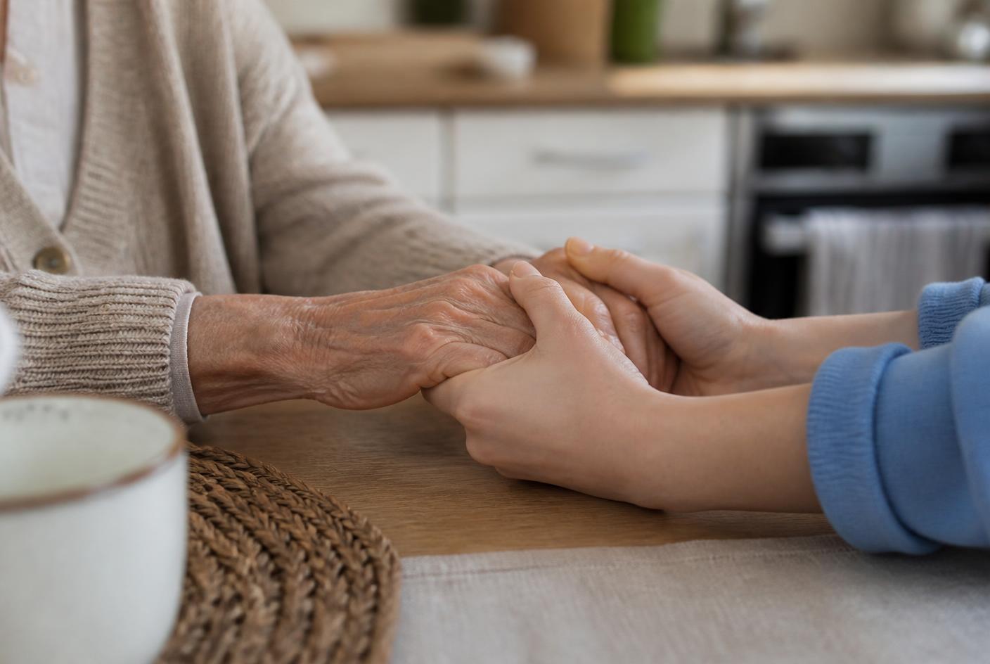 A caregiver and an older adult holding hands at a kitchen table